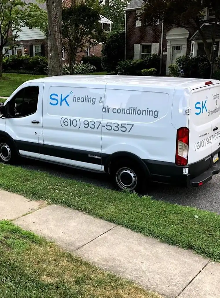 An SK Heating and Air Conditioning van parked on a Main Line street of brick colonial homes